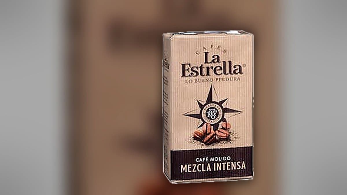 Dos paquetes de café molido La Estrella junto a una taza de café humeante sobre una encimera, luz matinal cálida