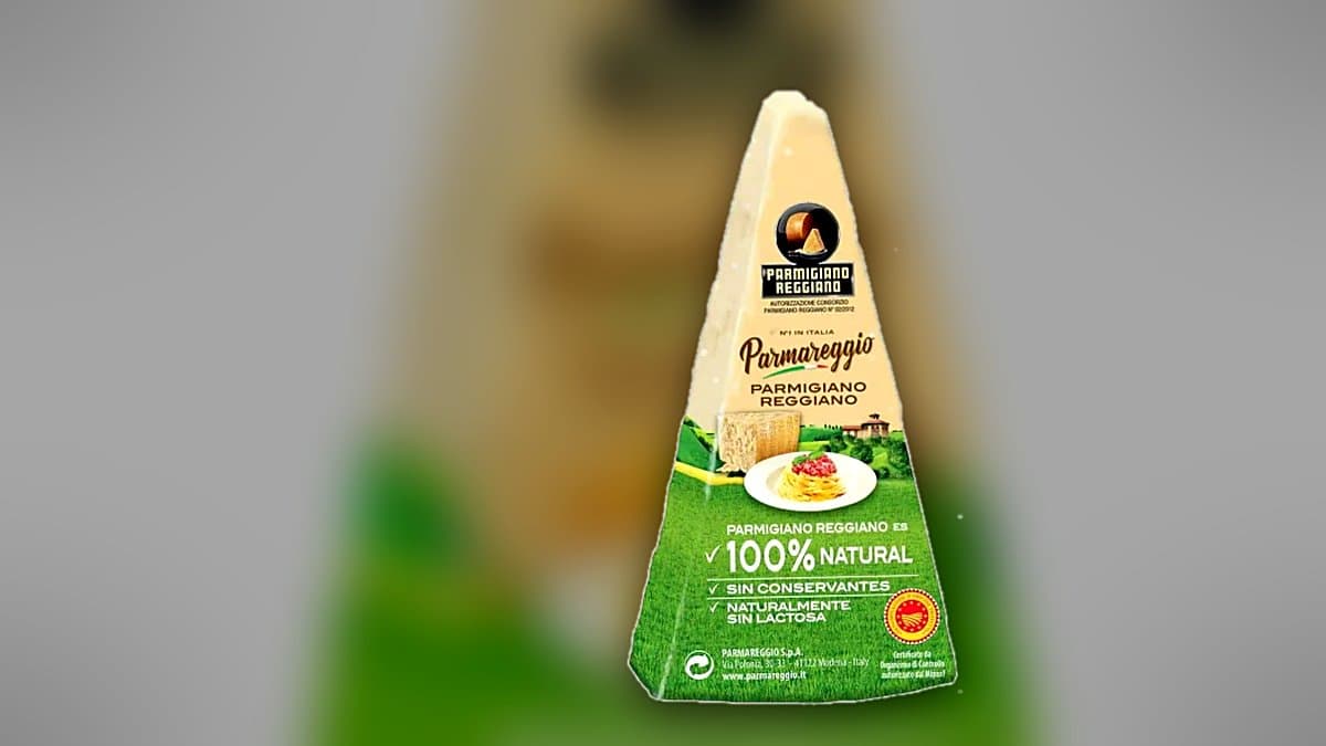 Wedge of Parmesan cheese with a grater and shavings on a rustic wooden board, Parmareggio package blurred in background, warm natural lighting