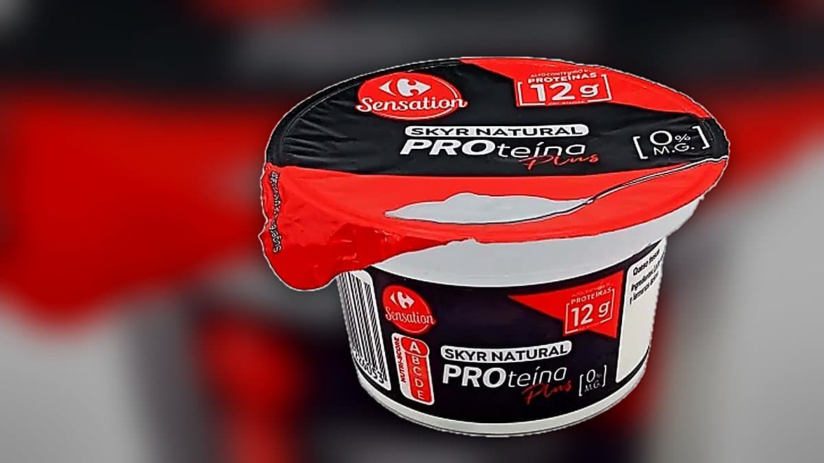 Bol de skyr islandés desnatado con frutos rojos y granola, junto a envase de Carrefour Sensation, luz mañana suave en mesa de madera