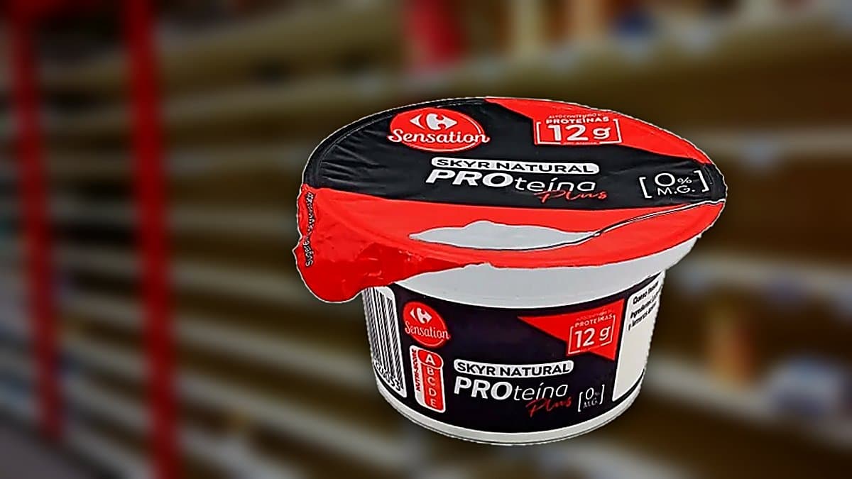 Bol de skyr islandés desnatado con frutos rojos y granola, junto a envase de Carrefour Sensation, luz mañana suave en mesa de madera