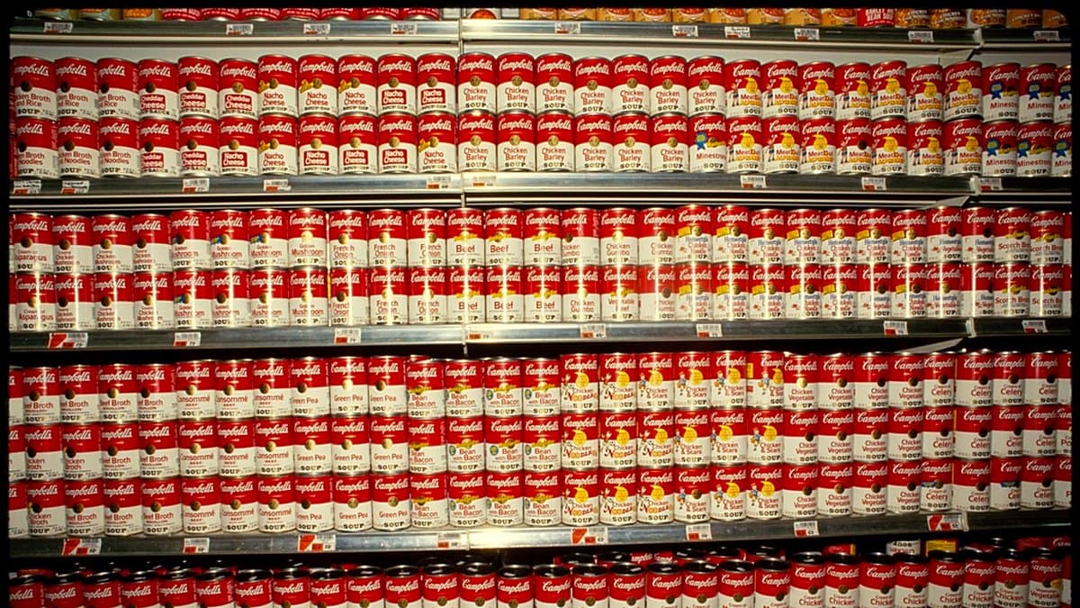 Aisle de supermercado con estantes de productos de colores, cliente empujando carrito, iluminación fluorescente de retail