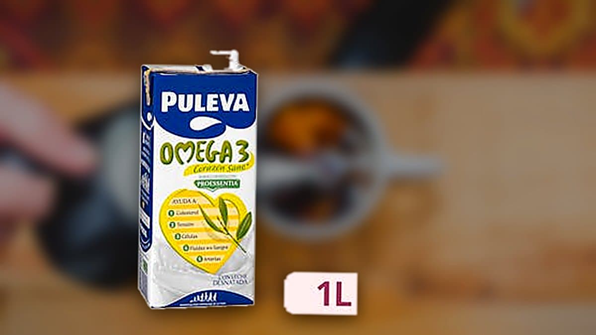 Cartón de leche Omega 3 desnatada Puleva de un litro sobre mesa de desayuno con luz natural matinal, vaso servido al lado, ambiente fresco y limpio.