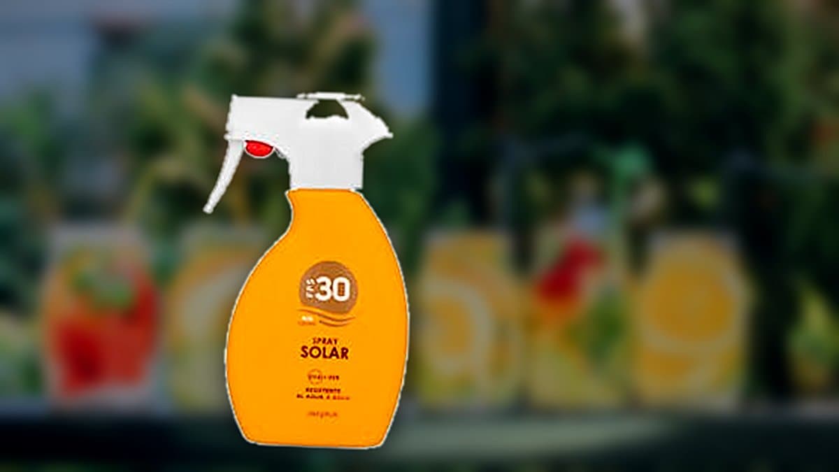 Botella de protector solar en spray sobre toalla de playa junto a gafas de sol y sombrero, luz de verano.