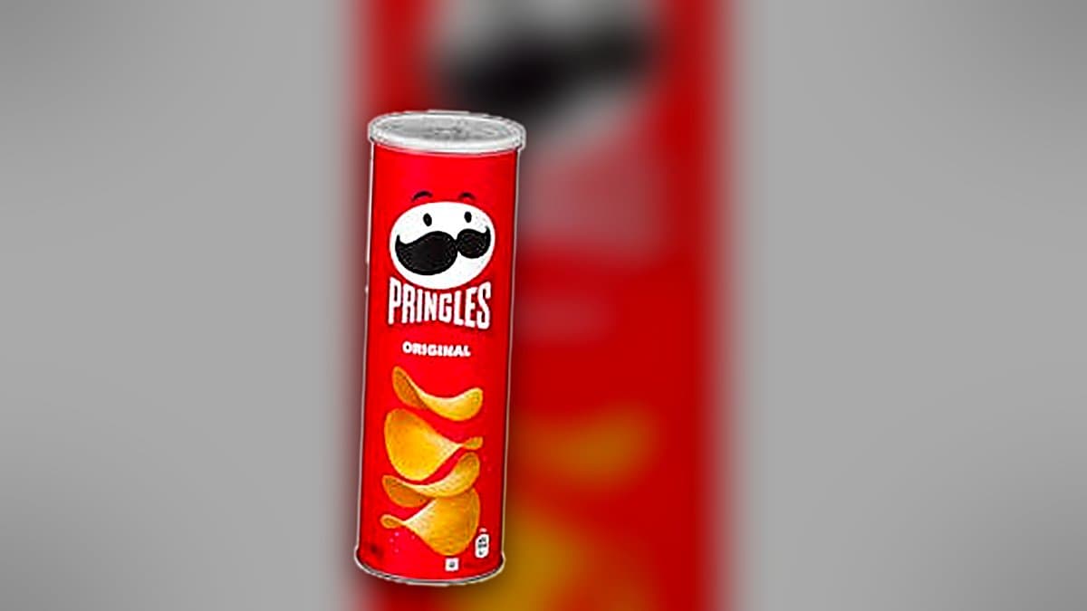 Bote de Pringles original tumbado en una mesa de picnic al atardecer, con patatas fritas esparcidas sobre la superficie