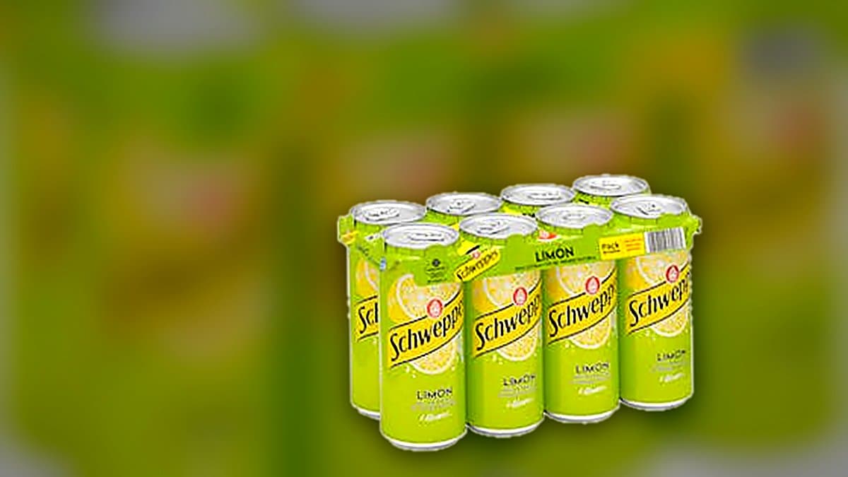 Botella grande de refresco de limón Schweppes con vaso helado y rodaja de limón en mesa de terraza con luz dorada