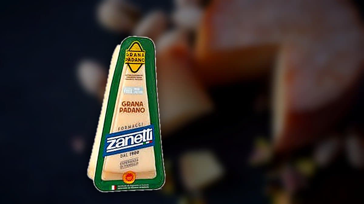 Cuña de queso grana padano sobre tabla de madera con rallador y plato de pasta fresca, cocina rústica