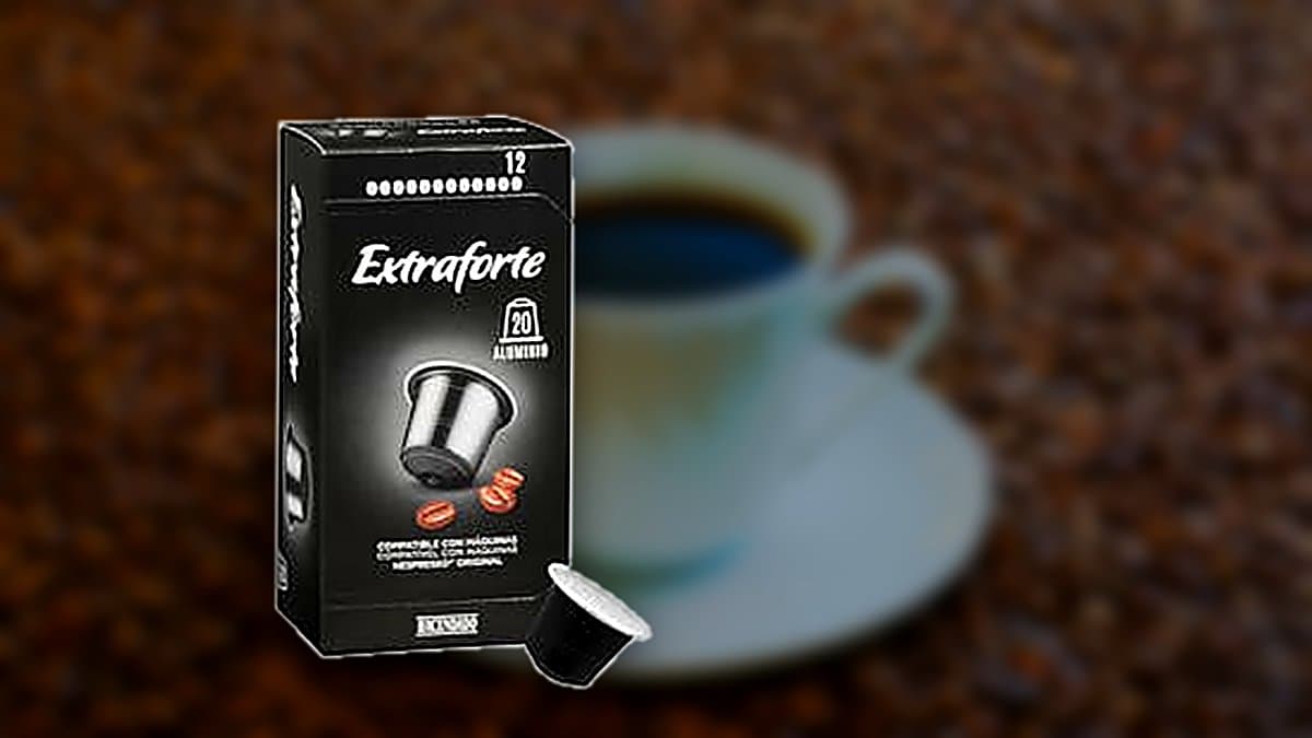 Cápsulas de café extra fuerte de Hacendado dispuestas junto a su caja de cartón sobre una mesa de madera oscura, con una taza de espresso con crema en primer plano.