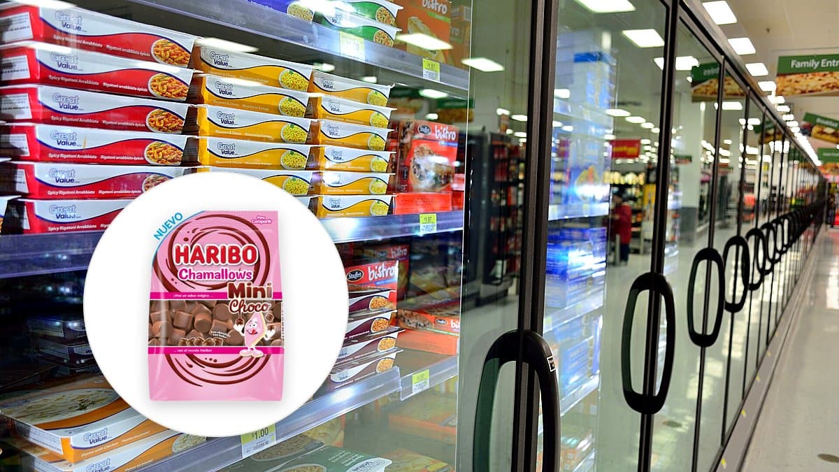 Manos sosteniendo un teléfono con buscador de productos en un pasillo de supermercado, estantes de lácteos y confitería de fondo