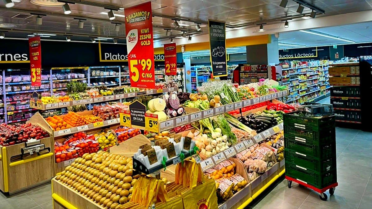 Persona sosteniendo una lista de compra escrita a mano frente a un carrito de supermercado con productos