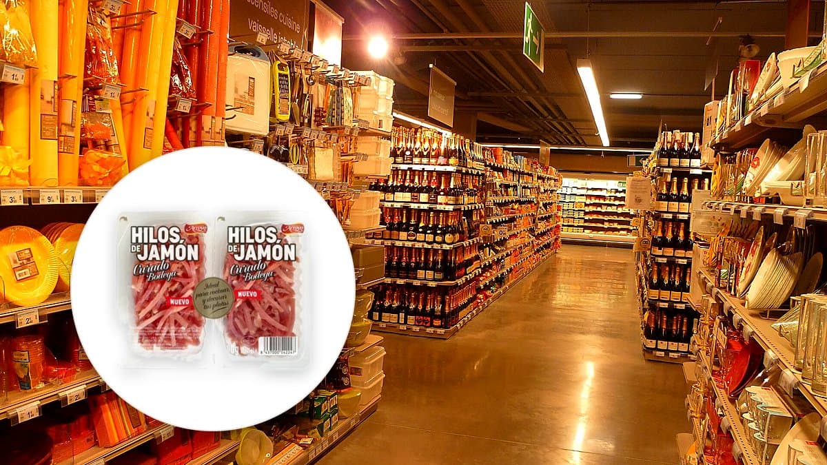 Dos pequeños sobres de jamón curado en hilos de Jamones Arroyo sobre una mesa de mármol, al lado de un bol de ensalada y palitos de pan, estilo supermercado