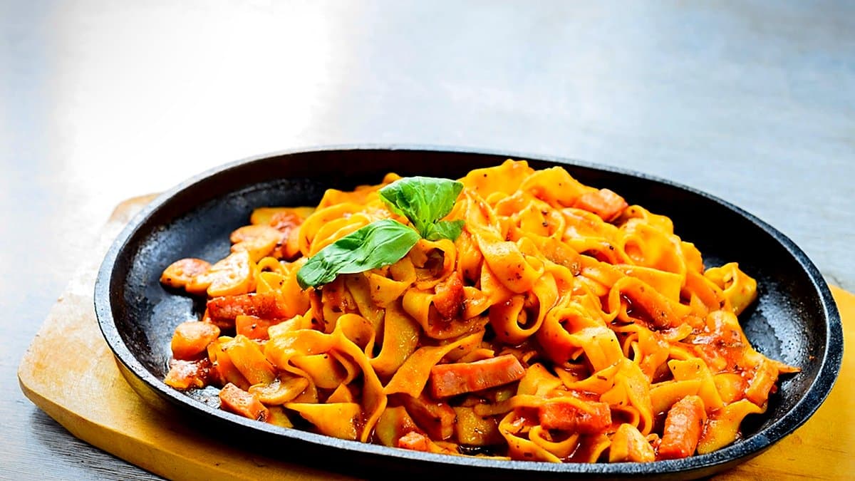 Estante de supermercado con paquetes de pasta y fideos variados, mano de cliente alcanzando un producto, iluminación cálida de tienda