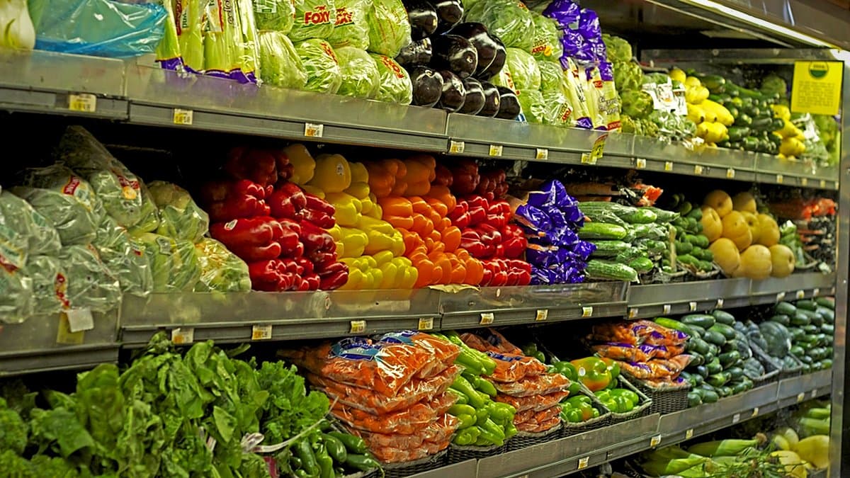 Sección de frescos en una tienda moderna con bandejas preenvasadas de pescado, frutas y verduras bajo iluminación cálida