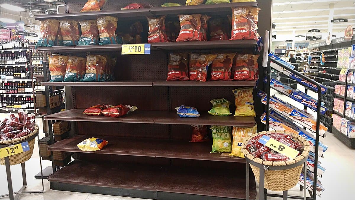 Recibo de supermercado enrollado sobre mesa con bolsa de compra abierta mostrando productos básicos, luz natural de mañana.