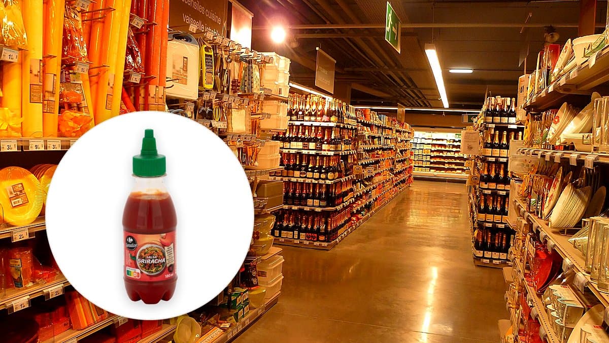 Bote pequeño de salsa sriracha Sensation de Carrefour junto a un bol de fideos y chiles rojos frescos en una cocina española.