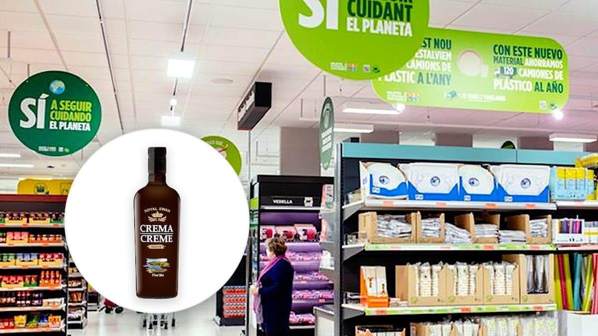 Botella de licor de crema Royal Swan junto a un vaso con hielo sobre mesa de madera, iluminación cálida de lámpara vespertina, ambiente acogedor desenfocado.