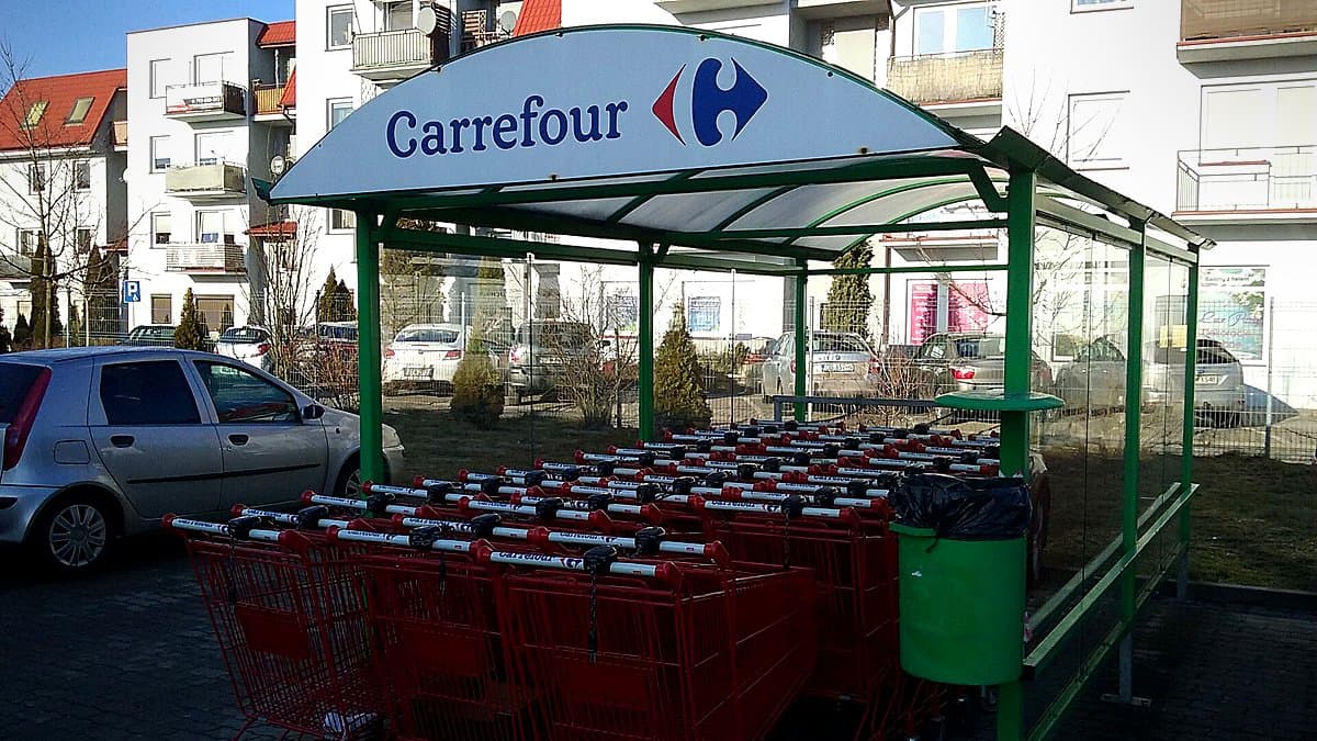 Carrito de compra español lleno de productos básicos de alimentación en pasillo de supermercado con luz natural de otoño temprano.